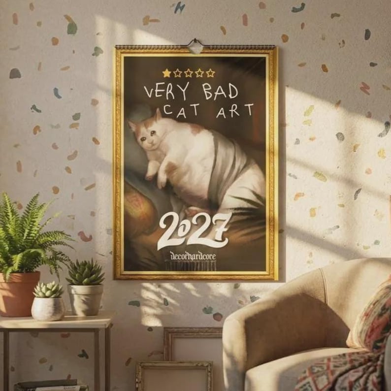May include: A wall calendar with a gold frame featuring a painting of a white and orange cat with a sad expression. The text reads "VERY BAD CAT ART" above a five-star rating, with "2027" in large white font and "decorhardcore" at the bottom.