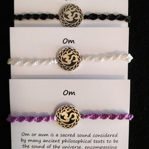 Puede incluir: Tres pulseras Om con cordones negros, blancos y morados. Cada pulsera tiene un dije de símbolo Om dorado. El texto "Om" está escrito en cada tarjeta y la tarjeta inferior incluye el texto "Om o aum es un sonido sagrado considerado por muchos textos filosóficos antiguos como el sonido del universo, que abarca todos los demás sonidos que hay en él."