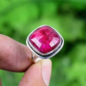 May include: A silver ring featuring a large, square-shaped, deep red ruby gemstone.