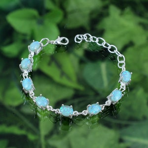 Peut inclure: Un bracelet en argent avec un design de chaîne et des pierres d'opale bleues de forme ovale.