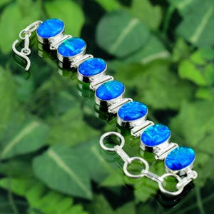 May include: A silver bracelet with oval blue opal stones. The opals are set in silver metal and linked together. The bracelet has a hook clasp. The opals display a vibrant, iridescent quality. The bracelet is approximately 18 cm in length.