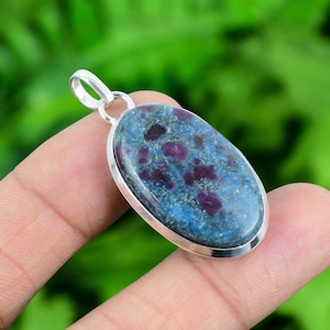 May include: Oval shaped pendant featuring a blue and purple gemstone set in sterling silver. The gemstone has a speckled pattern with small red inclusions.