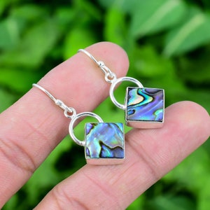 May include: A pair of silver earrings with square abalone shell pendants. The earrings have a simple hoop design and dangle from a silver hook.