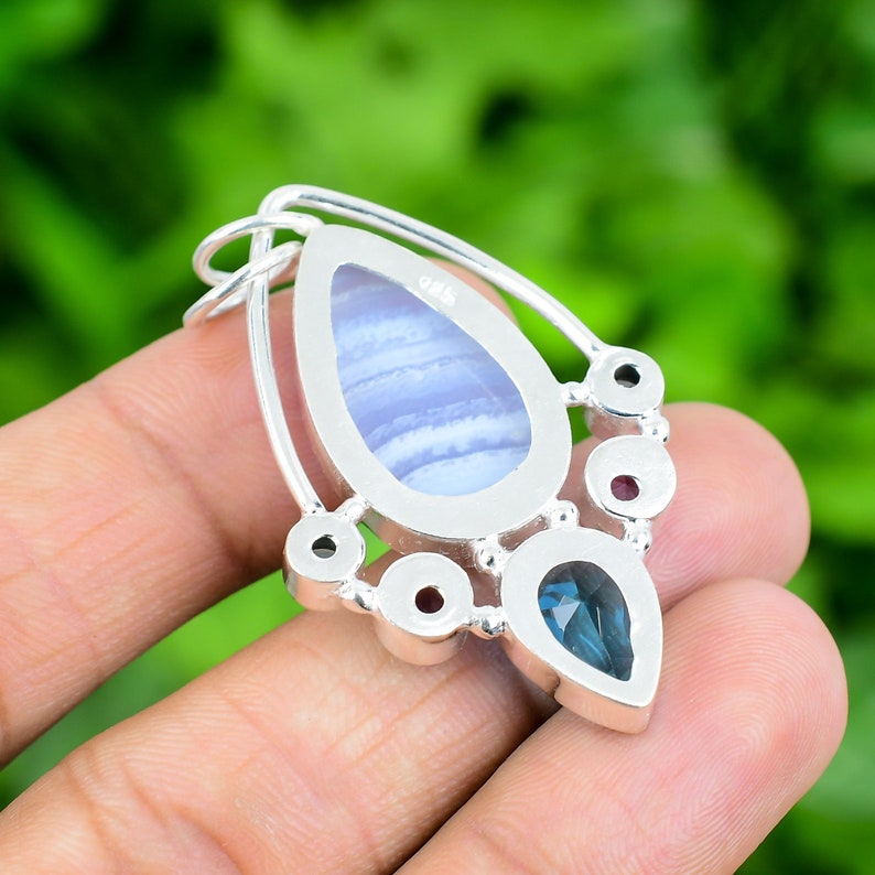 May include: Silver pendant featuring a blue agate stone and a blue topaz stone. The pendant is set in a silver frame with an ornate design. The pendant is marked "925" on the reverse.