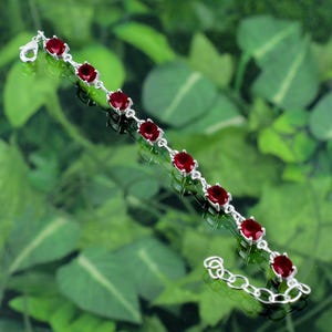 May include: A silver bracelet with a chain link design and red round gemstones.