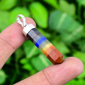 May include: A multi-colored gemstone pendant with a silver-colored bail. The pendant features a spectrum of colors, including shades of purple, blue, yellow, orange, and brown. The gemstone is faceted and has a polished finish.