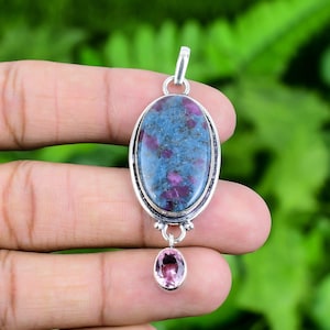 May include: A silver pendant with a blue and pink gemstone. The main stone is oval shaped and has a speckled pattern of pink and blue. The smaller stone is pink and round.