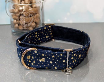 Puede incluir: Un collar para perro azul marino con estrellas doradas y una hebilla de metal dorado. El collar está acolchado y tiene un pequeño amuleto plateado.