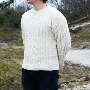 May include: A white cable knit sweater with a crew neck. The sweater has a textured pattern and is made of a soft, warm material.