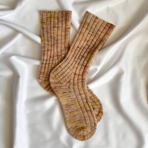 May include: A pair of brown and beige knitted socks with a ribbed texture. The socks are made of a soft, comfortable material and have a subtle colour variation.