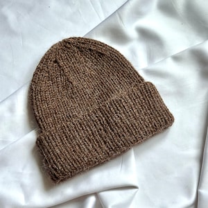 May include: A brown knitted beanie hat with a ribbed brim. The hat is made of a soft, fuzzy yarn and has a simple, classic design.
