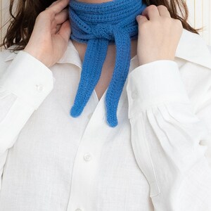May include: A woman wearing a white button-down shirt with a blue knitted scarf tied around her neck.