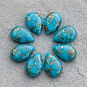Puede incluir: Siete piedras preciosas de turquesa en forma de lágrima dispuestas en un patrón circular. Cada piedra presenta un color azul vibrante con intrincadas vetas de matriz dorada que recorren las superficies pulidas y lisas de los cabujones.