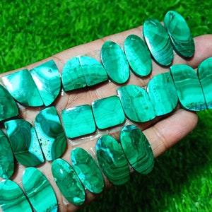 K&ouml;nnte beinhalten: Eine Sammlung von gr&uuml;nen und wei&szlig;en Malachit-Cabochons, einige oval und einige quadratisch, mit einer Vielzahl von Mustern und Texturen.