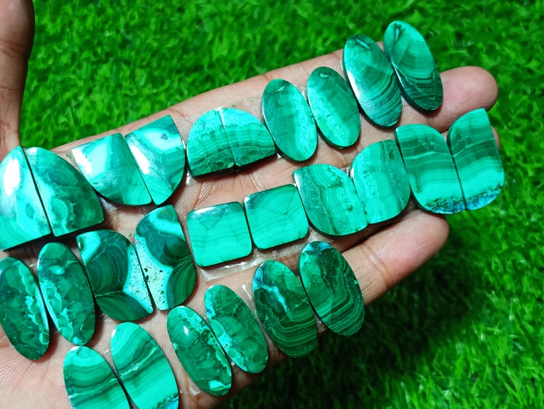 K&ouml;nnte beinhalten: Eine Sammlung von gr&uuml;nen und wei&szlig;en Malachit-Cabochons, einige oval und einige quadratisch, mit einer Vielzahl von Mustern und Texturen.