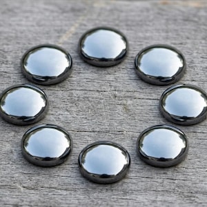 May include: Eight polished, metallic, round stones arranged in a circle. The stones have a reflective, silver-like surface and are set against a weathered, gray wooden background. The stones appear to be decorative.