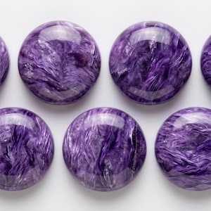 Peut inclure: Huit pierres précieuses rondes et polies avec un motif tourbillonnant et marbré dans des tons de violet et de blanc. Les pierres sont disposées en deux rangées sur une surface blanche, mettant en valeur leurs surfaces brillantes et réfléchissantes.