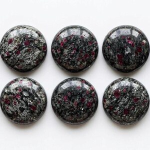May include: Ten circular cabochons arranged in two rows of five. Each piece features a polished, dark gray and black mottled stone surface with embedded, vibrant red crystalline inclusions scattered throughout the textured, mineral composition.