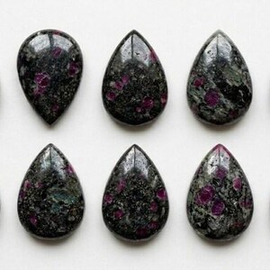 May include: Ten polished, teardrop-shaped cabochons arranged in two rows of five. Each stone features a dark, mottled black and deep green base with embedded, irregular magenta-colored inclusions throughout the smooth, reflective surface.