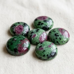 May include: Six polished gemstones with a mix of green and red colors. The stones have a rounded shape and are arranged in a circular pattern. The green areas have black speckles.