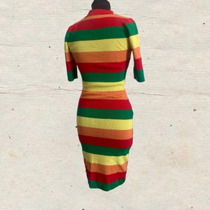 Puede incluir: Vestido ajustado, hasta la rodilla, con mangas cortas, expuesto en un maniqu&iacute;. El vestido presenta rayas horizontales en rojo, verde, amarillo y naranja. El vestido tiene un cuello alto y una textura de punto acanalado.