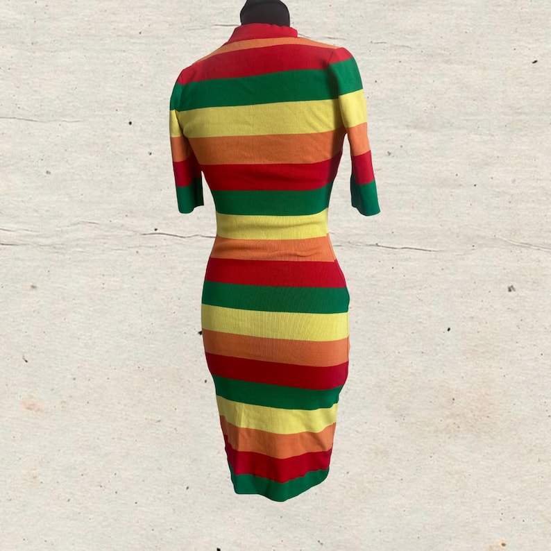 Puede incluir: Vestido ajustado, hasta la rodilla, con mangas cortas, expuesto en un maniqu&iacute;. El vestido presenta rayas horizontales en rojo, verde, amarillo y naranja. El vestido tiene un cuello alto y una textura de punto acanalado.