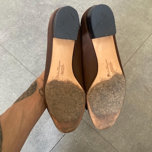 May include: A pair of brown leather flats with a pointed toe. The shoes have a leather sole and are marked "Salvatore Ferragamo" on the inside.