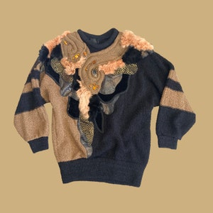 May include: A black and brown sweater with a large, decorative floral design. The design features faux fur, leather, and beads.