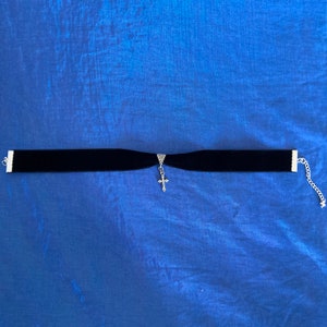 May include: A black velvet choker necklace with a silver cross pendant.