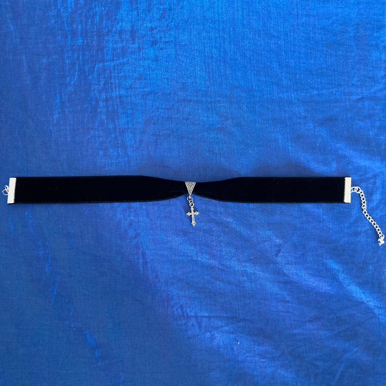 May include: A black velvet choker necklace with a silver cross pendant.
