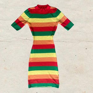 Puede incluir: Un vestido multicolor de manga corta con rayas horizontales rojas, naranjas, amarillas, verdes y un cuello alto rojo. El vestido es entallado y parece estar hecho de tejido de punto. El estilo general es retro y vibrante.