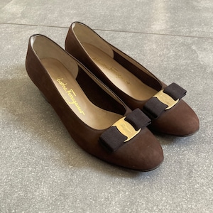 May include: A pair of brown suede ballet flats with gold buckles and black bows. The shoes are by Salvatore Ferragamo.
