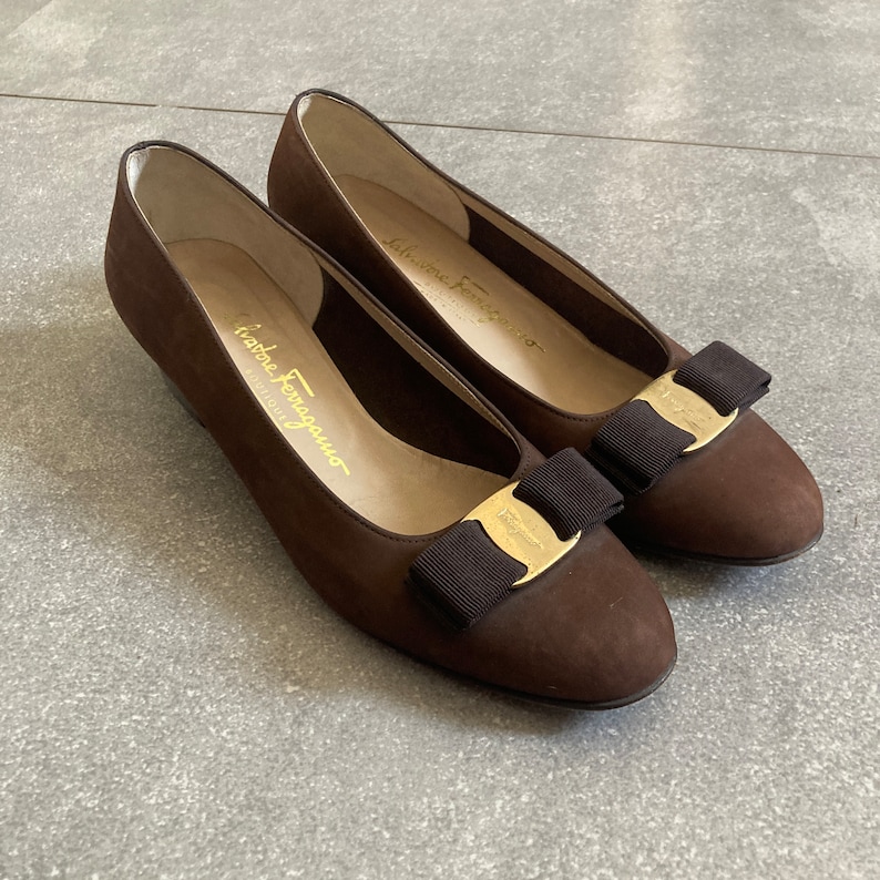 May include: A pair of brown suede ballet flats with gold buckles and black bows. The shoes are by Salvatore Ferragamo.