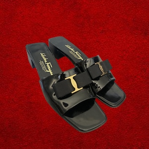 May include: Pair of black patent leather sandals with a square toe and small block heel. Each sandal features a black bow with a gold-tone buckle. The brand name "Salvatore Ferragamo" is printed on the insole.