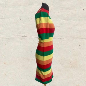 Puede incluir: Un vestido a rayas multicolores con cuello alto y mangas cortas. El vestido presenta bandas horizontales rojas, naranjas, amarillas y verdes. El vestido se exhibe en un maniqu&iacute;.