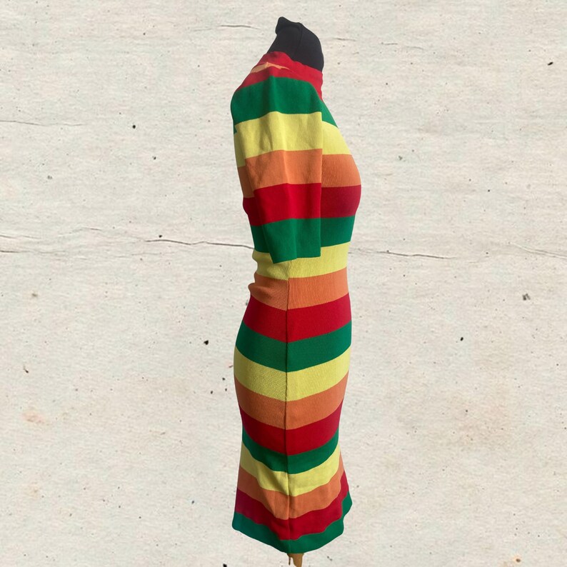 Puede incluir: Un vestido a rayas multicolores con cuello alto y mangas cortas. El vestido presenta bandas horizontales rojas, naranjas, amarillas y verdes. El vestido se exhibe en un maniqu&iacute;.