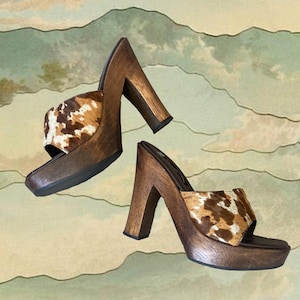 May include: A pair of brown wooden platform heels with a cowhide print. The heels are about 4 inches tall and have a chunky platform.