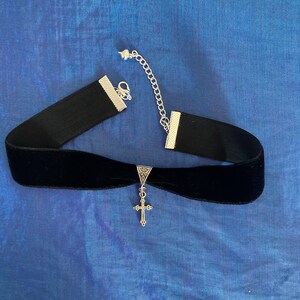 May include: A black velvet choker necklace with a silver cross pendant. The choker has a silver chain closure.
