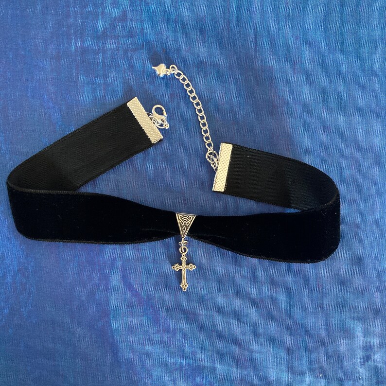 May include: A black velvet choker necklace with a silver cross pendant. The choker has a silver chain closure.