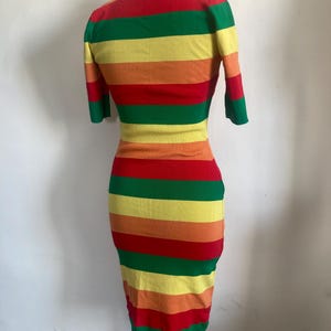 Puede incluir: Vestido ajustado a la figura con un patr&oacute;n de rayas arco&iacute;ris. El vestido tiene mangas cortas y un cuello alto. Las rayas alternan entre rojo, naranja, amarillo, verde y un amarillo m&aacute;s claro. Largo hasta la rodilla.