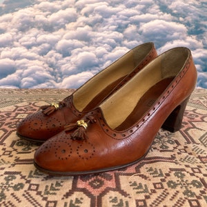 May include: A pair of brown leather heeled shoes with tassel details. The shoes have a brogue design and a pointed toe.