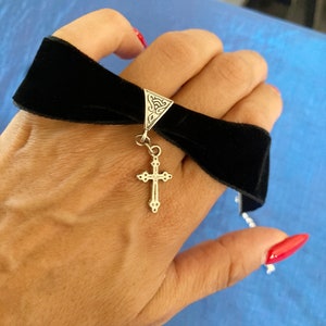 May include: A black velvet choker with a silver cross pendant and a triangular charm with an intricate design.