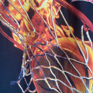 Puede incluir: Primer plano de una red de baloncesto con un dise&ntilde;o naranja y amarillo llameante. La red est&aacute; hecha de cuerda blanca y est&aacute; unida a un fondo negro.