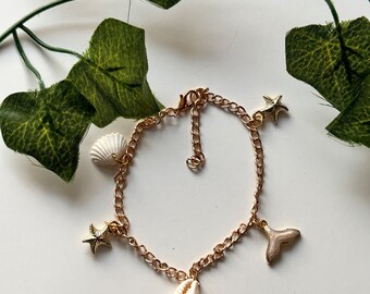 Op de afbeelding: Gouden kettingarmband met meerdere bedels, waaronder schelpen en zeesterren. De bedels zijn wit en goud.