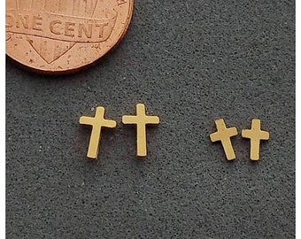 May include: Close-up of gold-colored cross earrings and a one-cent coin on a dark gray surface. Two pairs of cross earrings are visible, one pair larger than the other. The coin is a copper color and shows the words "ONE CENT".