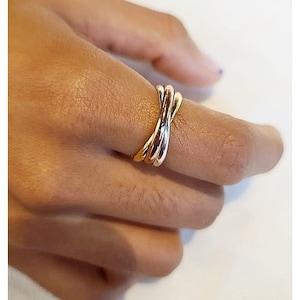 May include: A gold and silver-toned ring with a twisted design. The ring is worn on a finger, showcasing its intertwined bands. The jewelry piece has a polished finish, reflecting light. The ring is a fashion accessory.