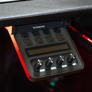 May include: A black Stream Deck with a small LCD screen and eight buttons. The deck has four knobs on the bottom and is mounted to a desk.