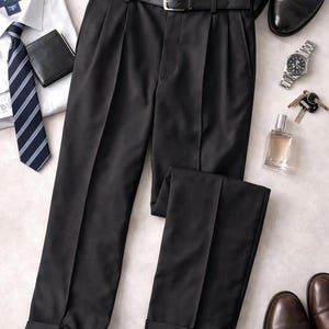 May include: A flat lay of men's formal wear, including black pleated trousers with a belt, a white dress shirt, a striped tie, a wallet, a wristwatch, keys, and a bottle of cologne. Two pairs of leather shoes are also present.