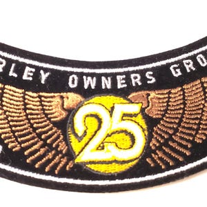 May include: A curved black embroidered patch featuring the text HARLEY OWNERS GROUP in white, with a central yellow circle containing the number 25, flanked by bronze-colored wings, and the years 1983 and 2008 stitched in white on the sides.