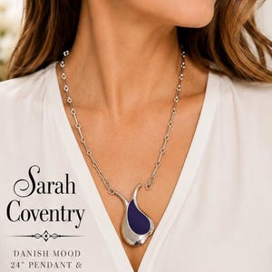 May include: A Sarah Coventry Danish Mood jewelry set featuring a silver-tone necklace with a 24-inch chain and a teardrop-shaped pendant with a dark blue inlay, accompanied by matching dark blue hoop earrings. The set is labeled as a 24-inch pendant and earrings set.